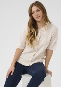 Svetloružový button-up kardigán s krátkymi rukávmi, pletenou štruktúrou a rebrovaným lemom. V kombinácii s tmavomodrými džínsami pre kontrast.