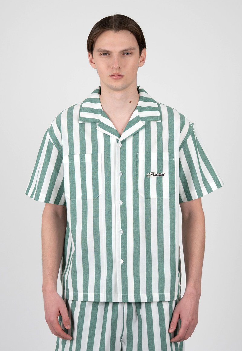 Jeune homme aux cheveux bruns lisses portant une chemise à manches courtes rayée verticalement verte et blanche et un short assorti, faisant face vers l'avant.