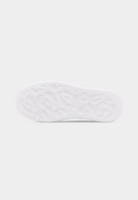 Λευκή σόλα παπουτσιού με ανάγλυφα αφαιρετικά και σχηματισμένα σαν γράμματα σχέδια σε επίπεδο ανοιχτό γκρι φόντο.