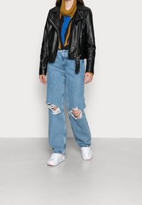 Czarna skórzana kurtka motocyklowa na wielokolorowym swetrze, zestawiona z jasnoniebieskimi podartymi dżinsami i białymi tenisówkami z różowymi akcentami.