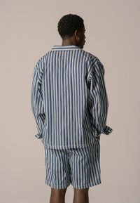 Completo loungewear in cotone con un design a righe blu e bianche, composto da una camicia con colletto e pantaloni corti coordinati, vestibilità comoda e maniche lunghe.