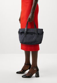 Marineblaues, gestepptes Handtasche mit strukturierter Form und zwei oberen Griffen. Ein markantes Steppmuster und Schnallenakzente fügen Details hinzu.