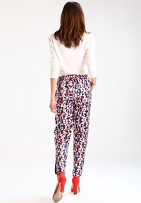 Pantalons de jogging à motifs en tissu doux, ornés de formes géométriques en rose, bleu marine et orange. Associés à des chaussures à talons rouges.