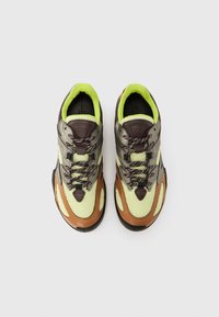 Limezöld hálós felsőrésszel, barna bőr részletekkel, fényvisszaverő ezüst díszítésekkel és sötét gumitalppal készült sportcipő. Mintás fűzőkkel.
