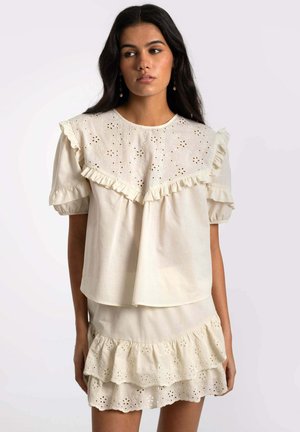 Top color crema con detalles de bordado de ojal, escote fruncido y mangas cortas abullonadas, combinado con una falda de capas a juego.
