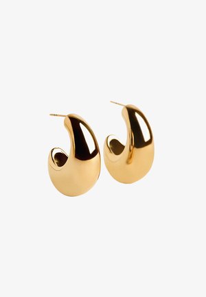 Złote metaliczne kolczyki w kształcie obręczy o gładkiej, lustrzanej powierzchni, zakrzywionym kształcie i otwartej przestrzeni w środku. Minimalistyczny design bez akcentów.
