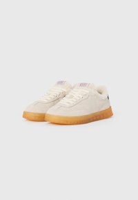 Sneakers in suede color beige chiaro con una fodera soffice, lacci bianchi e suole in gomma trasparente. Presentano un logo sulla linguetta.