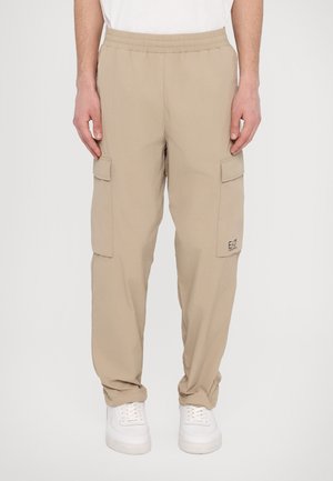 Pantalons cargo beige avec une taille élastique, deux poches cargo latérales et un logo discret sur la poche gauche. Fabriqués en tissu léger.
