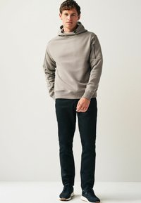 Lys grå hoodie med kengurulomme og justerbar snor i hætten, parret med sorte bukser og mørke sneakers. Glat stof, afslappet pasform.