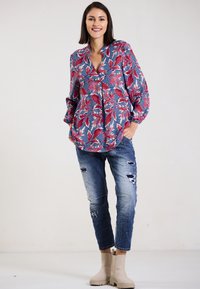 Floral blouse with red and blue leaves, paired with distressed light blue jeans and beige ankle boots. Relaxed fit and deep neckline.