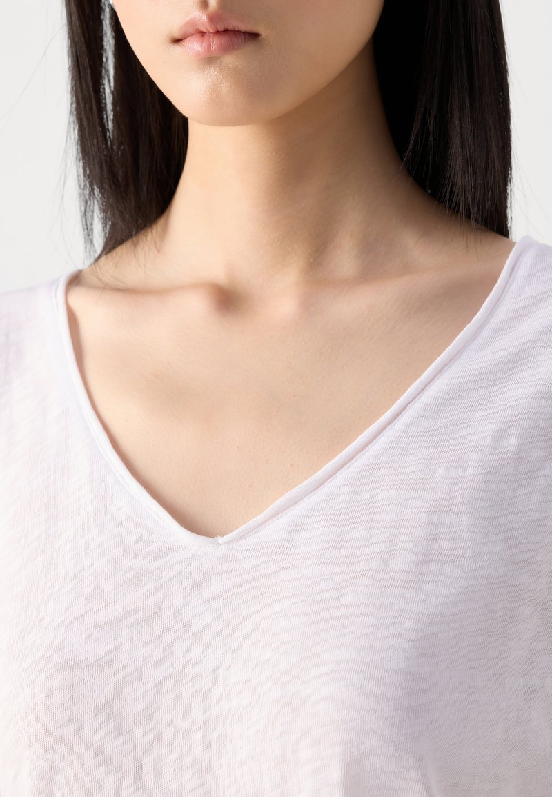 Biała bluzka z dekoltem w serek, wykonana z miękkiego materiału o lekko teksturowanym wyglądzie. Charakteryzuje się luźnym krojem, podkreślającym dekolt i ramiona.