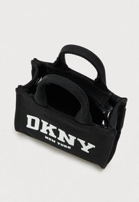 Μικρή μαύρη τσάντα υφάσματος DKNY New York με δύο λαβές και άνοιγμα με φερμουάρ στην κορυφή σε λευκό φόντο.