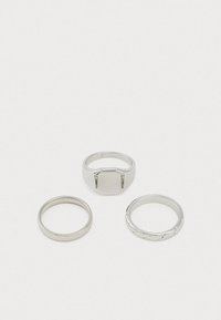 Conjunto de três anéis de prata: um anel superior largo e retangular, um clássico anel fino e um anel com design torcido. Acabamento em metal suave em todo o conjunto.