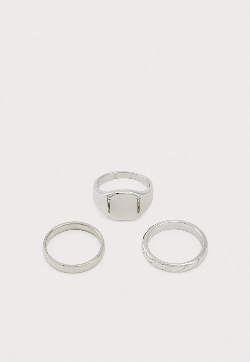 Conjunto de três anéis de prata: um anel superior largo e retangular, um clássico anel fino e um anel com design torcido. Acabamento em metal suave em todo o conjunto.