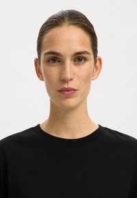 Black cotton t-shirt with a round neckline, featuring a soft texture and a simple design. The model's face is centered with natural makeup.