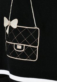 Tejido negro que presenta un diseño de bolso acolchado en hilo beis, adornado con un lazo. El bolso tiene forma rectangular y una tapa.