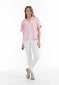 Lys rosa kortærmet bluse med V-hals, parret med hvide slim-fit bukser og grå hælede sandaler. Blødt, struktureret stof.