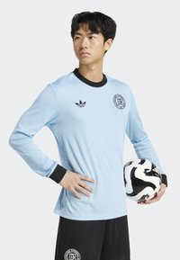 Lichtblauw langetermijn voetbalshirt met ribbelstructuur, zwarte kraag en manchetten, met een zwart logo. Zwarte shorts en een gestreepte voetbal.