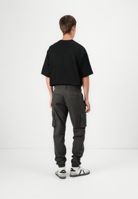 T-shirt noire surdimensionnée associée à un pantalon cargo gris avec poches latérales et poignets élastiques, porté avec des baskets blanches.