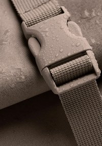 Grå textilrem med en formsprutad plastspänne, som visar vattendroppar på ytan. Har en strukturerad väv och robust design.