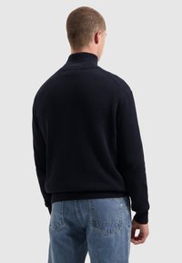 Marineblauwe geribde pullover met hoge kraag, voorzien van lange mouwen en een relaxte pasvorm, gecombineerd met lichtblauwe denim jeans.
