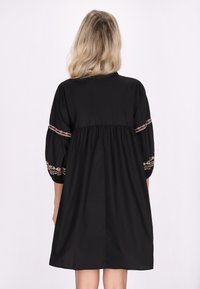 Rochie neagră cu o croială lejeră, având accente florale brodate pe mâneci și talie strânsă. Textură moale, design până la genunchi.