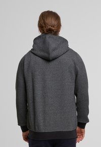 Felpa grigia con texture, dotata di cappuccio e polsini a coste. Presenta un sottile motivo geometrico e una vestibilità rilassata. Vista da dietro.