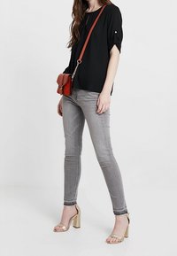 Musta lyhythihainen pusero käärittyine hihoineen, harmaat kapeat farkut ja kultaiset korkokengät. Punainen olkalaukku lisää värikontrastia.