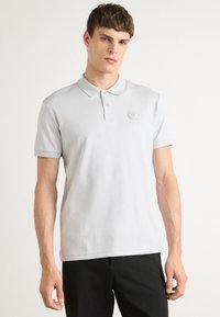 Polo cinza em tecido suave, com colarinho clássico, lista de três botões e logotipo hexagonal em relevo no lado esquerdo do peito.