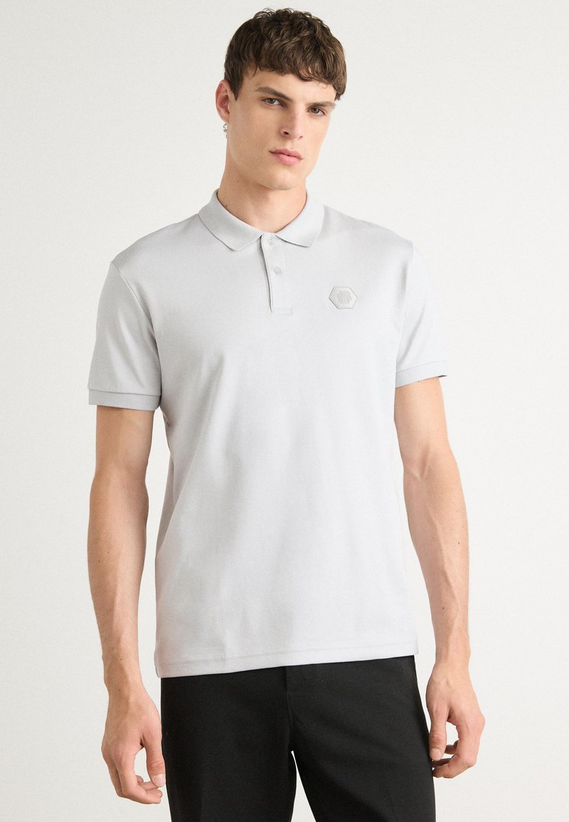 Polo cinza em tecido suave, com colarinho clássico, lista de três botões e logotipo hexagonal em relevo no lado esquerdo do peito.