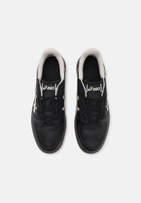 Baskets de sport noires avec des accents blancs, en matériau synthétique lisse, à lacets, avec des détails perforés au niveau des orteils. Logo sur la languette.