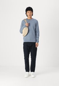 Light blue textured sweater, black pants, and white sneakers. A cream-colored crossbody bag hangs from the left shoulder.
