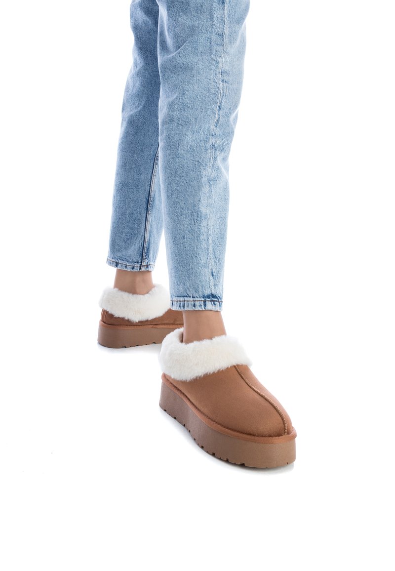 Zapatillas marrones con un suave collar de piel sintética blanca, con una suela gruesa y un sencillo detalle de costura, combinadas con unos vaqueros de color azul claro.