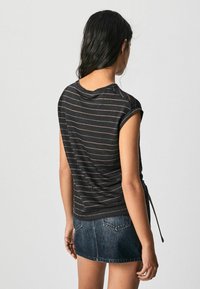 Sortstribet kortærmet top med opsmøg, der har en afslappet pasform og en buet kant, som ties i siden. Båret med en denimnederdel.