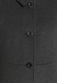 Ciemnoszara wełniana kurtka z wyciętym kołnierzem, z czarnymi guzikami i gładką fakturą. Charakteryzuje się prostymi liniami i minimalistycznym wzornictwem.