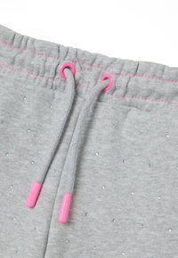 Grijze joggingbroek met elastische taille, roze oogjes, trekkoord en versieringen van kleine, sprankelende blauwe en groene rhinestones verspreid over de broek.