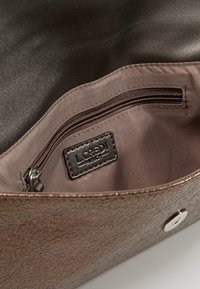 Intérieur de sac à main marron texturé avec une poche zippée, comprenant une doublure en tissu et une étiquette en cuir de marque. Fermeture à bouton métallique présente.