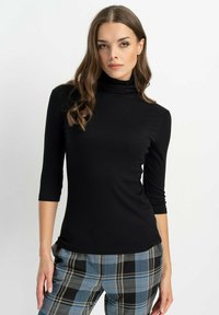Schwarzes, geripptes Rollkragenoberteil mit Dreiviertelärmel, figurbetontem Design und glatter Textur, kombiniert mit karierter Hose in Blau und Grau.
