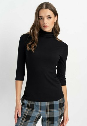 Schwarzes, geripptes Rollkragenoberteil mit Dreiviertelärmel, figurbetontem Design und glatter Textur, kombiniert mit karierter Hose in Blau und Grau.