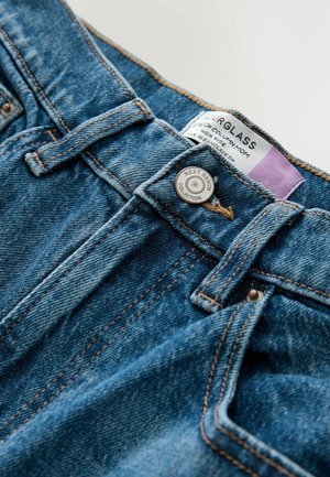 Džíny z denimu s vysokým pasem, modrá wash, výrazné švy, kovové zapínání a štítek označený "NEXT DENIM COLLECTION."