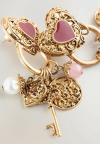 Goldfarbene Ohrringe mit herzförmigen Anhängern und rosa Emaille-Mittelpunkten, aufwendigen Verzierungen und einem dekorativen Schlüsselanhänger mit einer Perlenakzent.