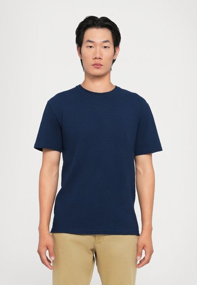 T-shirt en coton bleu marine à manches courtes, col rond et coupe standard. Présente un discret logo près de l'ourlet.