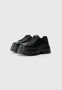 Black lace-up platform shoes with a chunky sole. Smooth leather upper, round toe, and a textured, sculpted outsole.