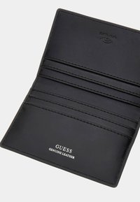 Portefeuille en cuir noir véritable avec des emplacements pour cartes et un logo embossé. Texture lisse avec des coutures blanches et un design minimaliste.