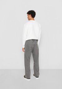 Pantalones de mezclilla gris de corte holgado, con una altura media y detalles de costura sutiles. Combinados con una camisa blanca de mangas largas y zapatos oscuros.