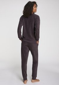 Temno purpurna flis udobna obleka, ki vključuje pulover s krožno ovratnikom in usklajene tapered hlače. Gladka tekstura in rebrasti obročki na rokavih in gležnjih.