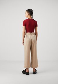 Rode aansluitende top met korte mouwen, gecombineerd met losse beige wijde broek met een volants tailleband. Zwarte platform sandalen met uitsparingen.