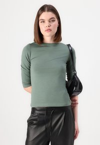 Grön långärmad topp i mjukt material, med en figursydd design. Kombinerad med högmidjade svarta läderbyxor och en liten svart väska.
