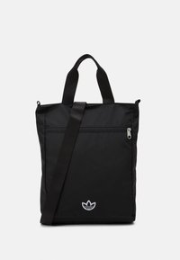 Sac fourre-tout en nylon noir avec deux poignées supérieures et une bandoulière. Il est doté d'une poche avant zippée et d'un accent logo blanc.