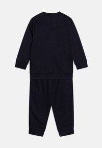 Tuta in cotone blu navy con top a maniche lunghe e chiusura a bottoni al collo, abbinato a pantaloni elasticizzati con polsini.